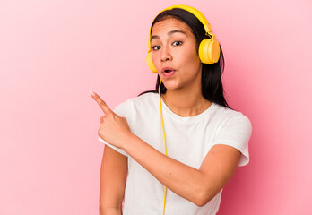 Young Venezuelan woman listening to music isolated on pink background pointing to the side