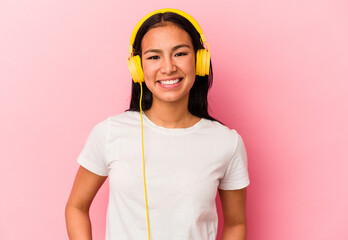 Young Venezuelan woman listening to music isolated on pink background happy, smiling and cheerful.