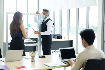 Fototapeta premium Caucasian boss and Asian teamwork is wearing mask for preventing covid19 virus and brainstorming in meeting room at office. Healthcare and New normal lifestyle in business concept. Focus at asian man.