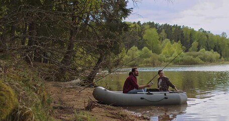 Young fishermen on an inflatable boat on the lake are fishing. Cinematic shot.