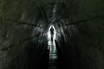 Lonely passerby man in a dark tunnel. Light at the end of the tunnel.