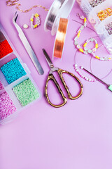 Creative flatlay of different seed and pearl beads with tools for making jewelry, wire string, scissors and necklace isolated on pink background.