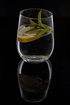 Vertical image of a gin and tonic with mint and lemon on a reflective black background 