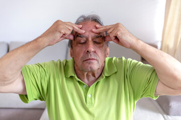 Relaxed modern 70 years old man at modern home in sunny summer day applying facial cream and making massage. Wrinkled old man with grey hair massaging his face around eyes, aging process.