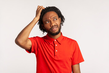 Doubt, need to think. Bearded man with dreadlocks wearing red casual style T-shirt, scratching head...