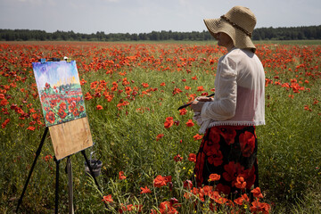 Mature woman artist paints a picture from nature on a field of blooming poppies