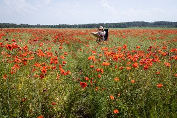 Mature woman artist paints a picture from nature on a field of blooming poppies, overall plan.