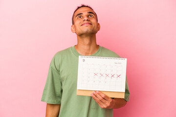 Young venezuelan man holding a calendar isolated on pink background dreaming of achieving goals and...