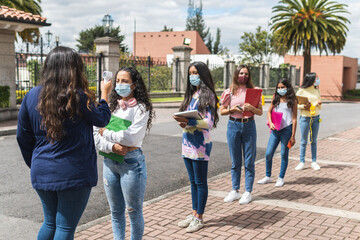 Line at the entrance of a school to check the temperature of the students with an infrared thermometer. Latina female teacher and students