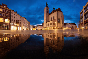 Fototapeta na wymiar Kirche Neupfarrplatz zur blauen Stunde mit Spiegelung in einer Wasserpfütze