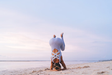 Slim woman standing upside down on beach