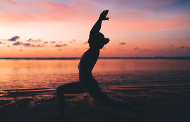 Unrecognizable slim woman performing yoga pose on embankment during sunset