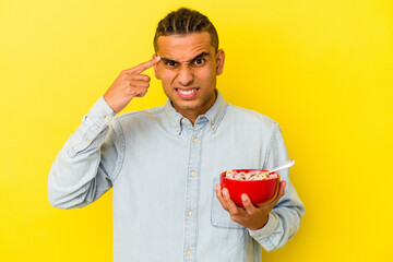 Young venezuelan man holding a cereals bowl isolated on yellow background showing a disappointment gesture with forefinger.