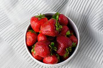 Juicy strawberries in a white plate. Fresh ripe delicious strawberries in a white bowl on a gray cloth background.