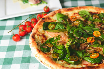 Delicious pizza with spinach and tuna shavings served on wooden table with green plaid tablecloth.