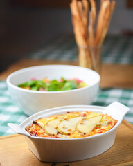 Cottage cheese and potato casserole with pears served in a white casserole dish and vegetable salad on the background.