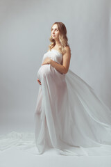 Elegant pregnant young woman standing wearing flying white fabric. Pregnancy, maternity and motherhood concept.