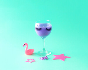 Glass cup with eyelashes and women's pink props. Celebration. Female party. Turquoise background.