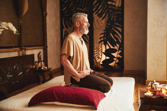 Tranquil seniour male practicing meditation in eastern studio