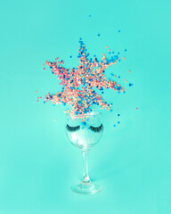 A glass with eyelashes from which he exposes sequins in height. A party, a women's celebration. Minimal composition.