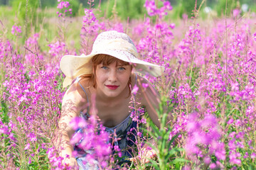 Young woman in a field of flowers wearing a straw hat on a hot summer day. Selective focus. Portrait