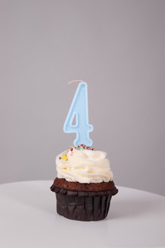 tasty chocolate cupcake with white topping cream and candle in shape of number four 4. on a white stand on a gray background. sweets, bakery. party food. dessert
