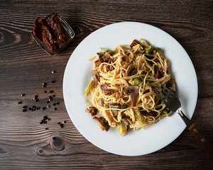Pasta with broccoli, mushrooms, dried tomatoes in cream sauce on a dark background