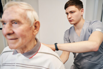 Focused orthopedic surgeon doing a back massage to pensioner