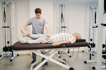Physical therapist pulling old male right leg during treatment activity