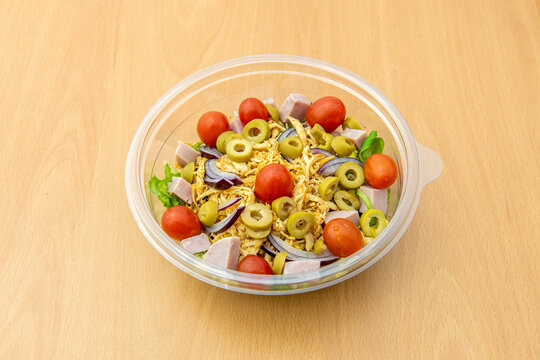 Pulled chicken salad with sliced green olives, diced ham, cherry tomatoes, iceberg lettuce and red onion in a home delivery container