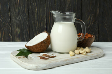Pitcher of milk, coconut and nuts on white wooden table