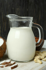 Pitcher of milk, coconut and nuts on white cutting board