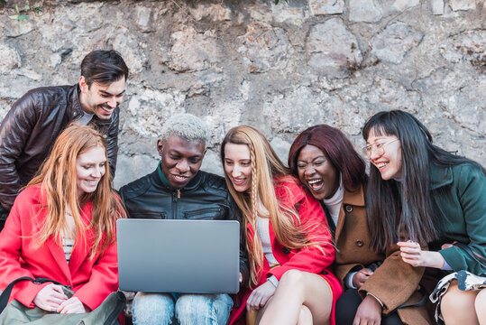 Group of multiracial friends gathering around laptop