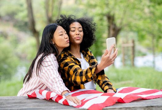 LGBT multiracial girlfriends taking selfie on smartphone in forest - Powered by Adobe