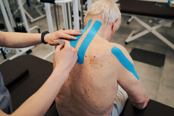 Manual therapist adding second kinesio tape to upper back