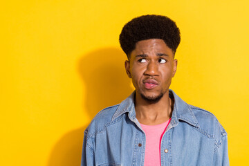 Photo of doubtful unsure dark skin guy dressed denim shirt looking empty space isolated yellow color background