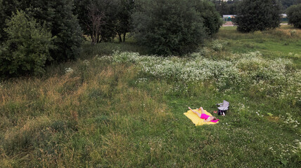 Obraz na płótnie Canvas A girl in a pink bathing suit sunbathes on a yellow rug. Around green grass and white flowers. Aerial photography.