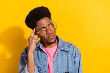 Photo of minded young dark skin man look empty space think wear glasses isolated on yellow color...