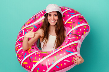 Young caucasian woman with an inflatable donut isolated on blue background person pointing by hand to a shirt copy space, proud and confident
