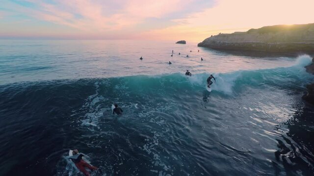 Aerial: Surfers catching waves in the ocean during sunset at Steamer Lane. Santa Cruz, California, USA