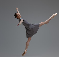 Attractive ballerina in gray dress dancing inside studio