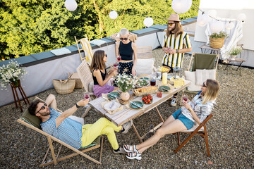 Young group of stylish people having a festive dinner on the roof terrace. Friends hanging out and having great summertime together outdoors