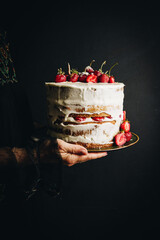 Woman in black embroidered dress holding strawberry and mascarpone layered Victoria sponge cake on...