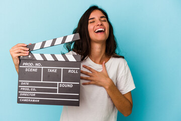 Young caucasian woman holding a clapperboard isolated on blue background laughs out loudly keeping...