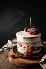Strawberry and mascarpone layered Victoria sponge cake with one candle on old wooden table on dark background.