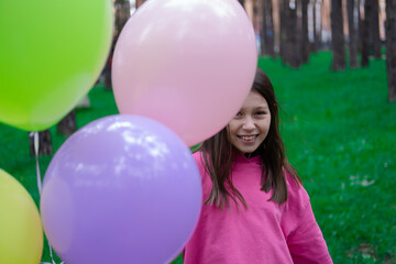 Fototapeta na wymiar sweet tween brunette girl in pink holding colorful balloons outdoors. party, birthday concept. summertime. happy kids