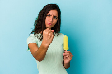 Young caucasian woman holding an ice cream isolated on blue background showing fist to camera,...