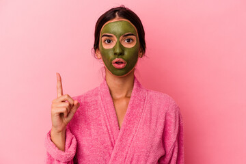 Young caucasian woman wearing a bathrobe and facial mask isolated on pink background having some great idea, concept of creativity.