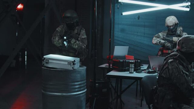 Slowmo tracking shot of SWAT team in uniform raiding dark hackers hideout They are checking laptops, computers and briefcase