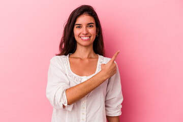 Fototapeta premium Young caucasian woman isolated on pink background smiling and pointing aside, showing something at blank space.